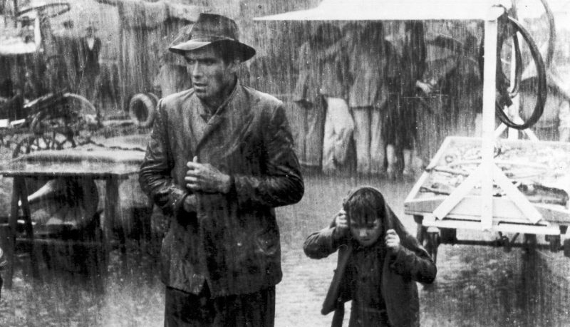 Un bărbat și un copil mergând prin ploaie